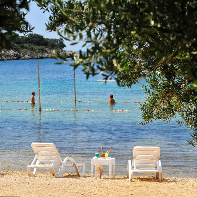 Plaža ispred objekta Lastura Resort s ležaljkama i mrežom za odbojku u mirnoj uvali Dubac.